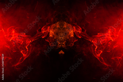 Smoke of different orange and red colors in the form of horror in the shape of the head, face and eye with wings on a black isolated background. Soul and ghost in mystical symbol