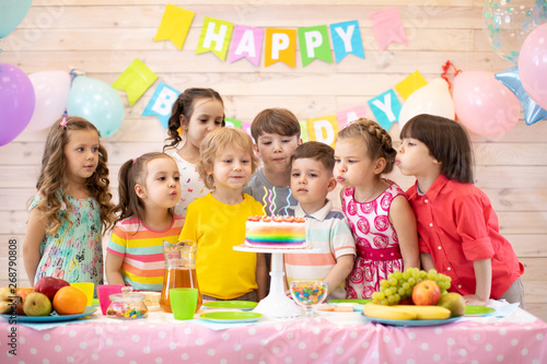 Group of kids celebrate birthday party and blow candles on festive cake