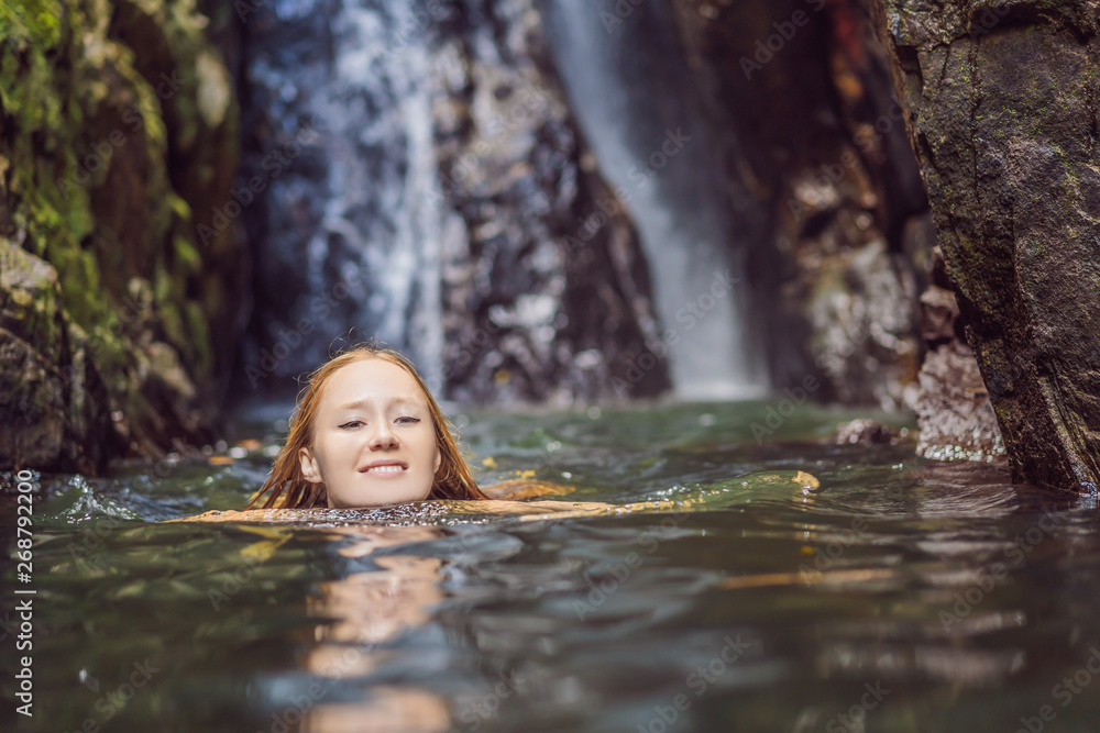 Fototapeta premium Young beautiful woman standing in the water at the waterfall