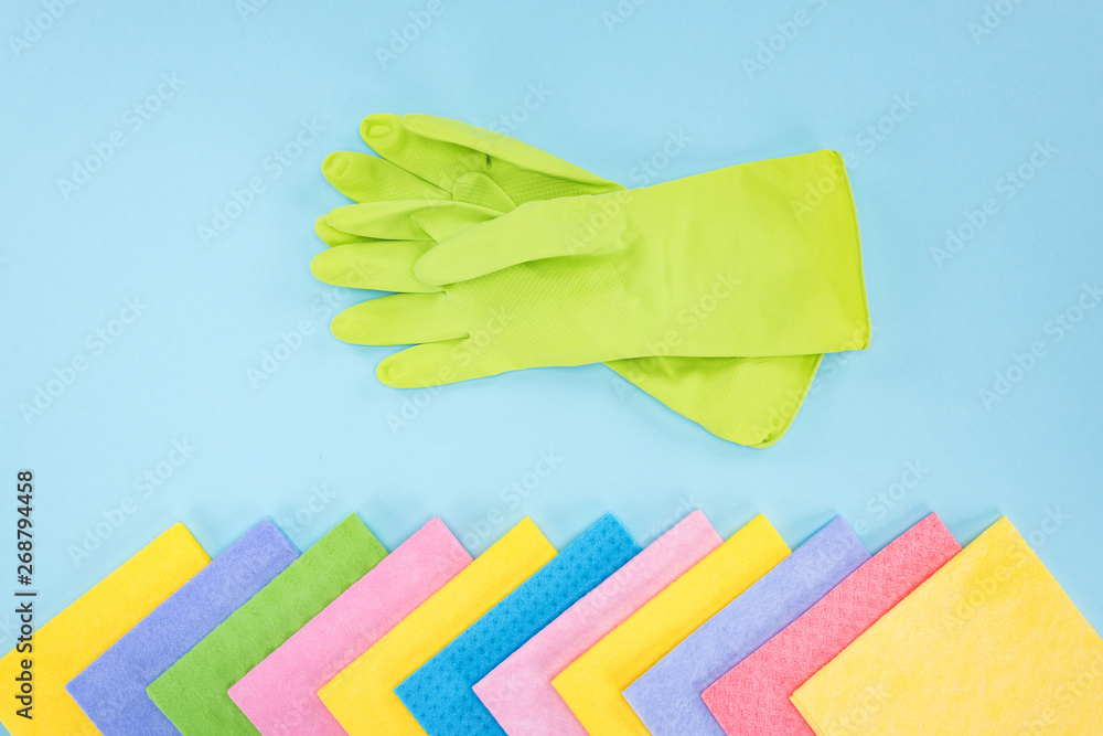 top view of green rubber gloves and multicolored rags on blue background top view of green rubber gloves and multicolored rags on blue background