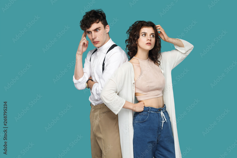 Portrait of two confused thoughtful brunette stylish partner standing, looking away, scratching head and thinking that to do and trying to find answer. indoor studio shot isolated on blue background. Portrait of two confused thoughtful brunette stylish partner standing, looking away, scratching head and thinking that to do and trying to find answer. indoor studio shot isolated on blue background.