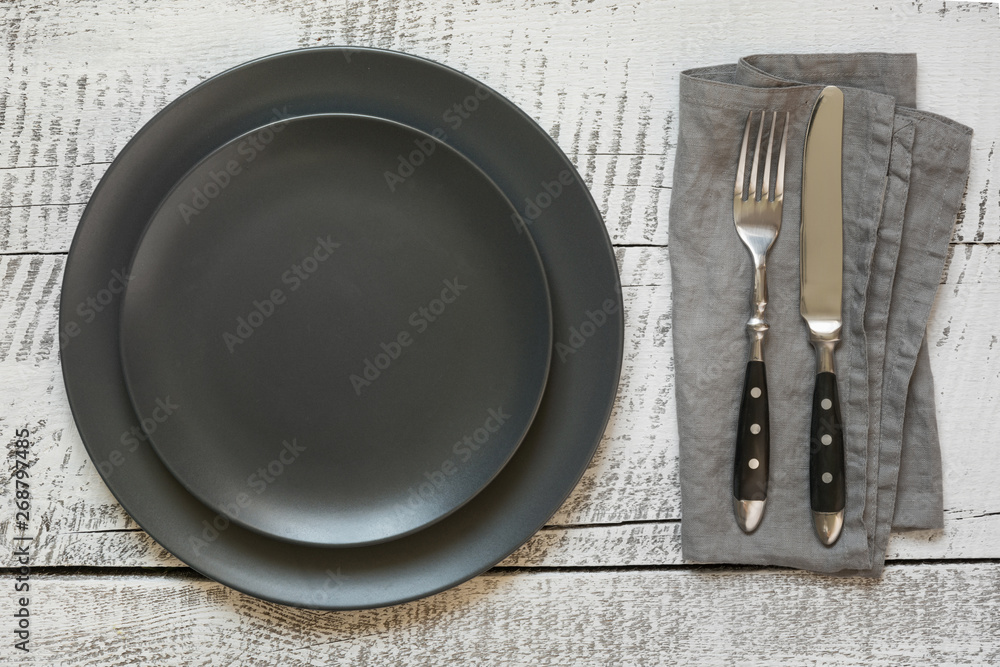 Table place setting with black plate on white wooden table. Top view. Table place setting with black plate on white wooden table. Top view.