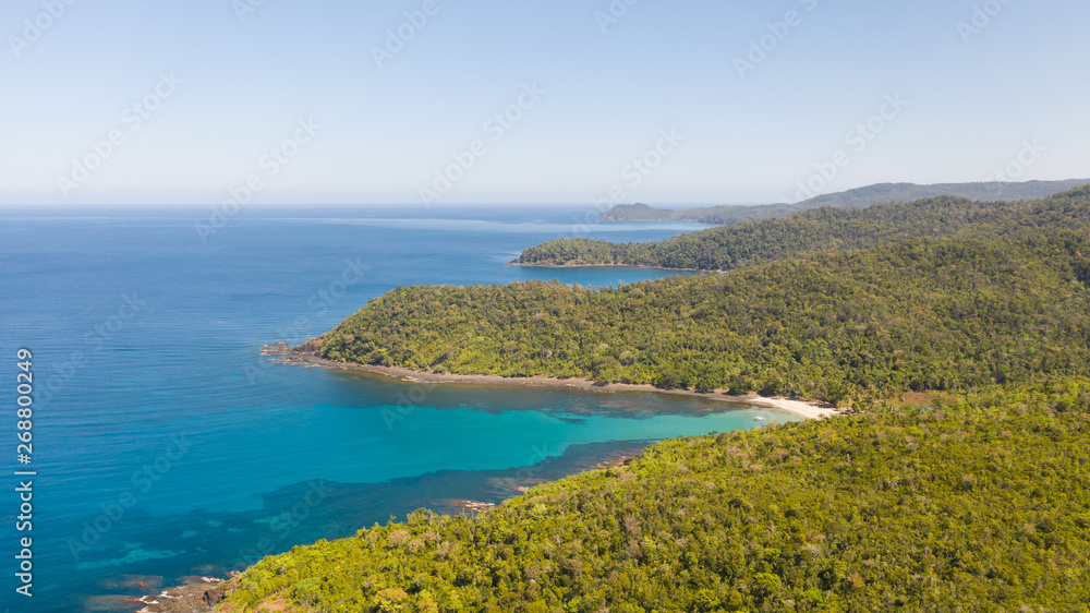Sea bay with turquoise water and a small white beach.Coast of the island of Camiguin, Philippines.Beautiful lagoon and volcanic island covered with dense forest, view from above.