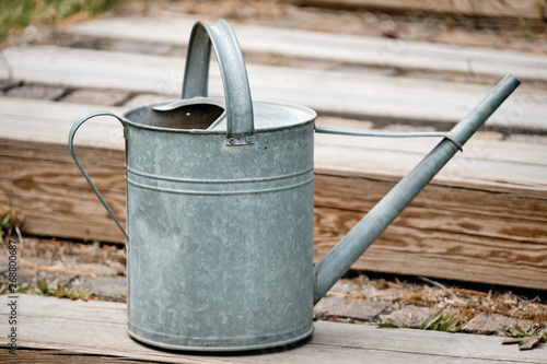 Old metal watering can standing on the wooden stairs of a terrace in the garden