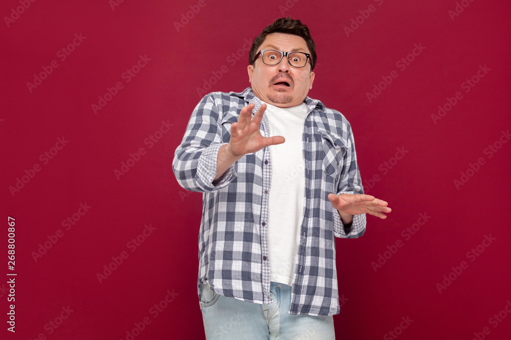 Portrait of shocked handsome middle aged business man in casual checkered shirt and eyeglasses standing and looking at camera with scared eyes. indoor studio shot, isolated on dark red background. Portrait of shocked handsome middle aged business man in casual checkered shirt and eyeglasses standing and looking at camera with scared eyes. indoor studio shot, isolated on dark red background.