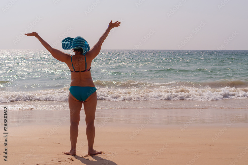 Happy elderly woman in a hat with raised hands on a background of the sea at sunset. Concept of sunny and happy summer. Happy elderly woman in a hat with raised hands on a background of the sea at sunset. Concept of sunny and happy summer.