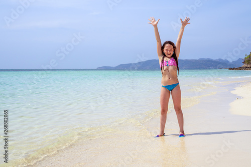 Happy child with hands up against the ocean with copy space. Concept of sunny and happy summer.