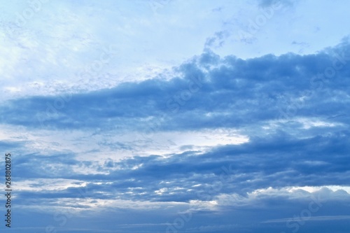 Blue sky with diagonal stripes of blue clouds. From left to right up. Photo with a blue gradient, from light to dark.