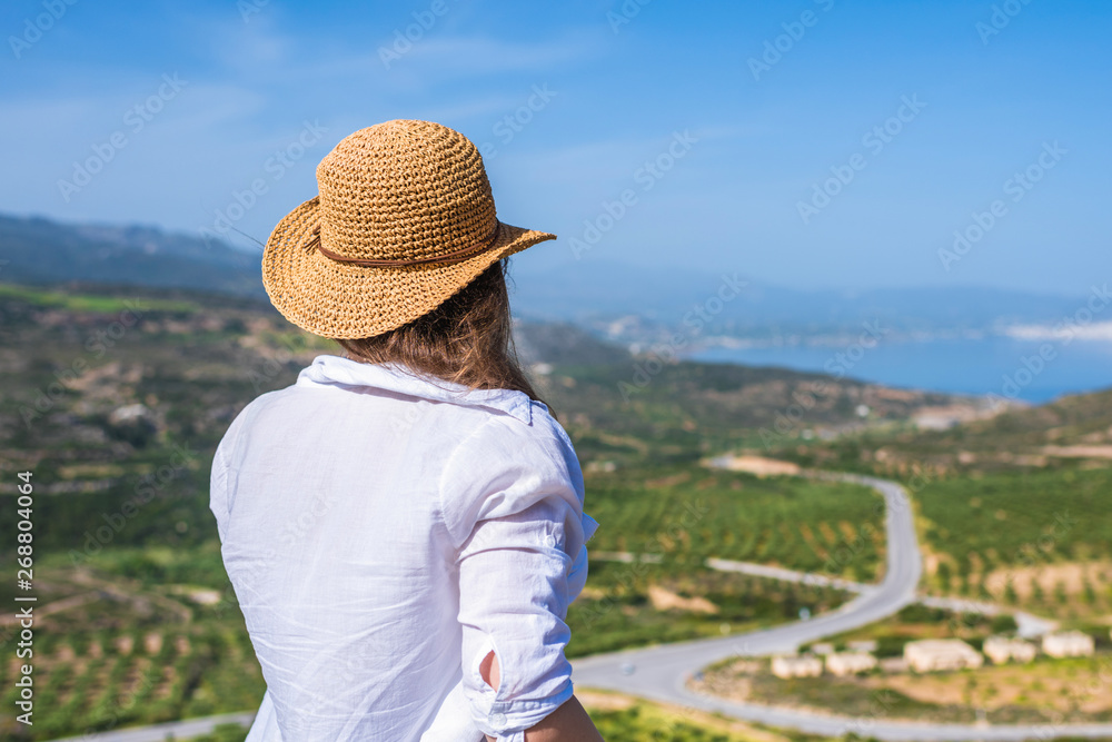 Woman in tourist clothes and straw hat standing on top of a mountain. Concept