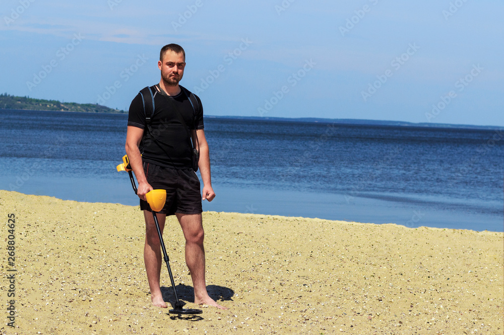 guy in shorts with a metal detector walking on the beach guy in shorts with a metal detector walking on the beach