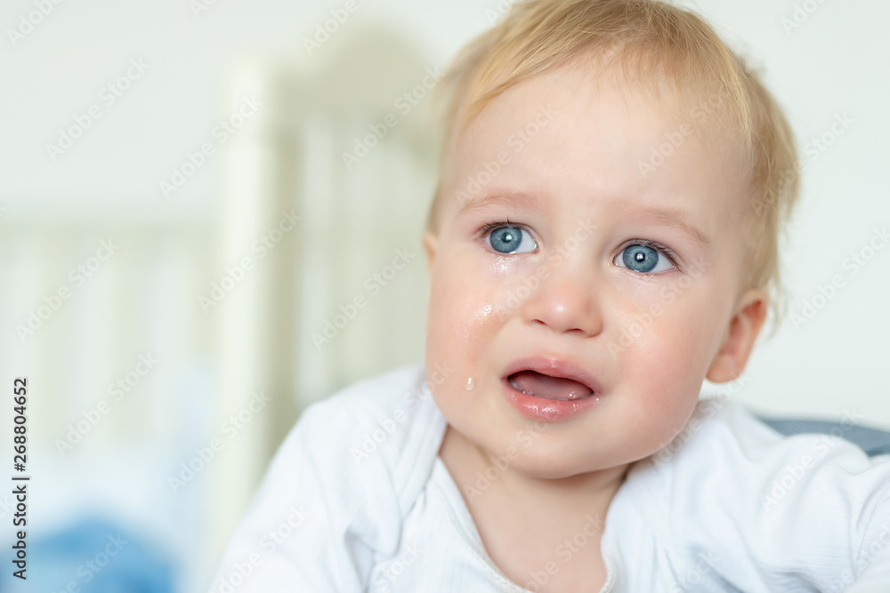 Cute caucasian blond toddler boy portrait crying at home during hysterics. Little child feeling sad. Small pensive baby after quarell