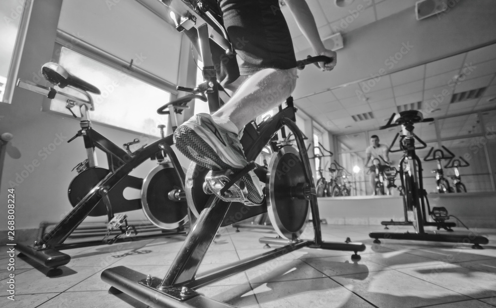 Obraz premium Wide angle view of man in sports sneakers and shorts does exercises on cardio bike at spinning class. Healthy lifestyle concept