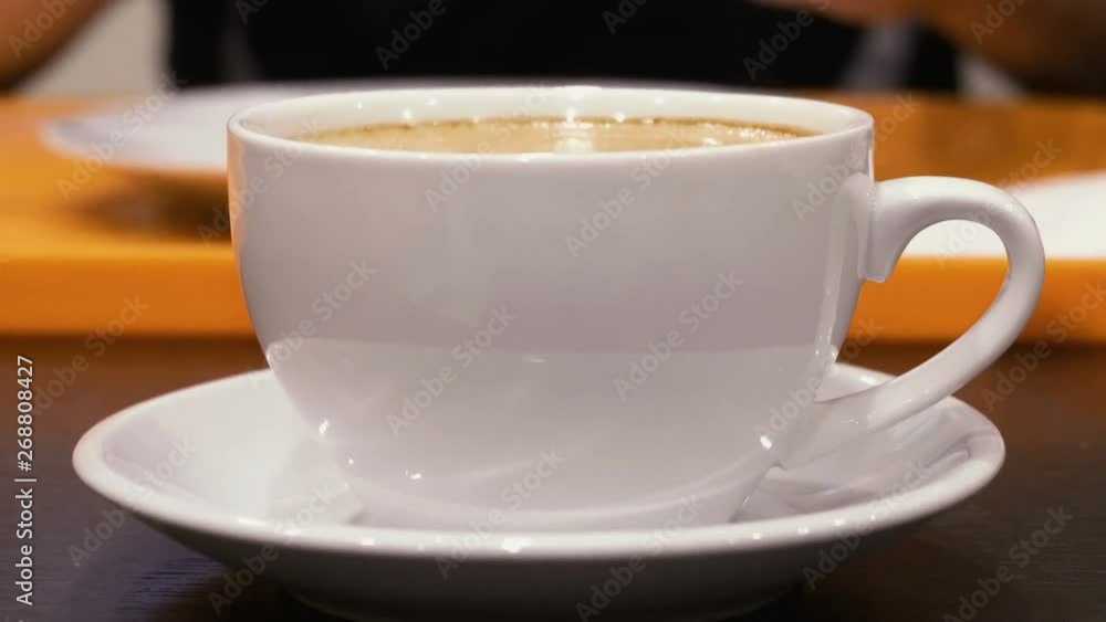 White mug with hot cappuccino coffee on the table. Steam rises up. Mug close up. White mug with hot cappuccino coffee on the table. Steam rises up. Mug close up.