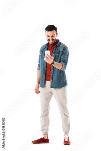 irritated man in denim shirt using smartphone isolated on white