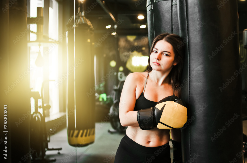 Tired fit woman resting after training near heavy bag at boxing room. Female boxer relaxing after workout
