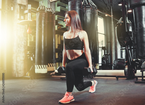 Training legs at the gym. Attractive fit woman doing lunges with dumbbells.