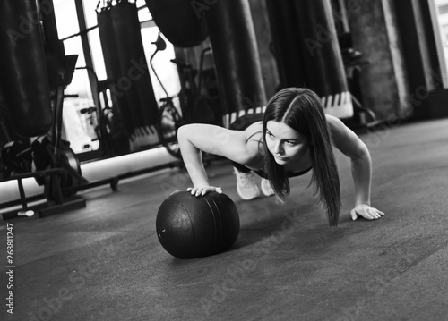 Woman doing push ups whith medicine ball  at dark gym