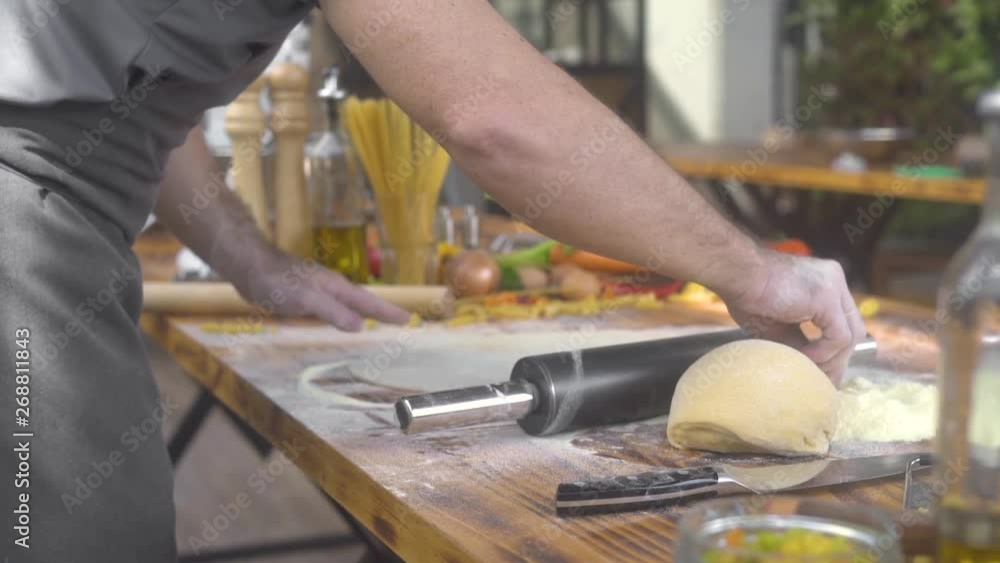 Chef cook sprinkling flour on pizza dough while rolling with roller pin. Man making dough for fresh pasta in italian restaurant. Cooking homemade pastry, cake and pie. Healthy homemade food. Chef cook sprinkling flour on pizza dough while rolling with roller pin. Man making dough for fresh pasta in italian restaurant. Cooking homemade pastry, cake and pie. Healthy homemade food.