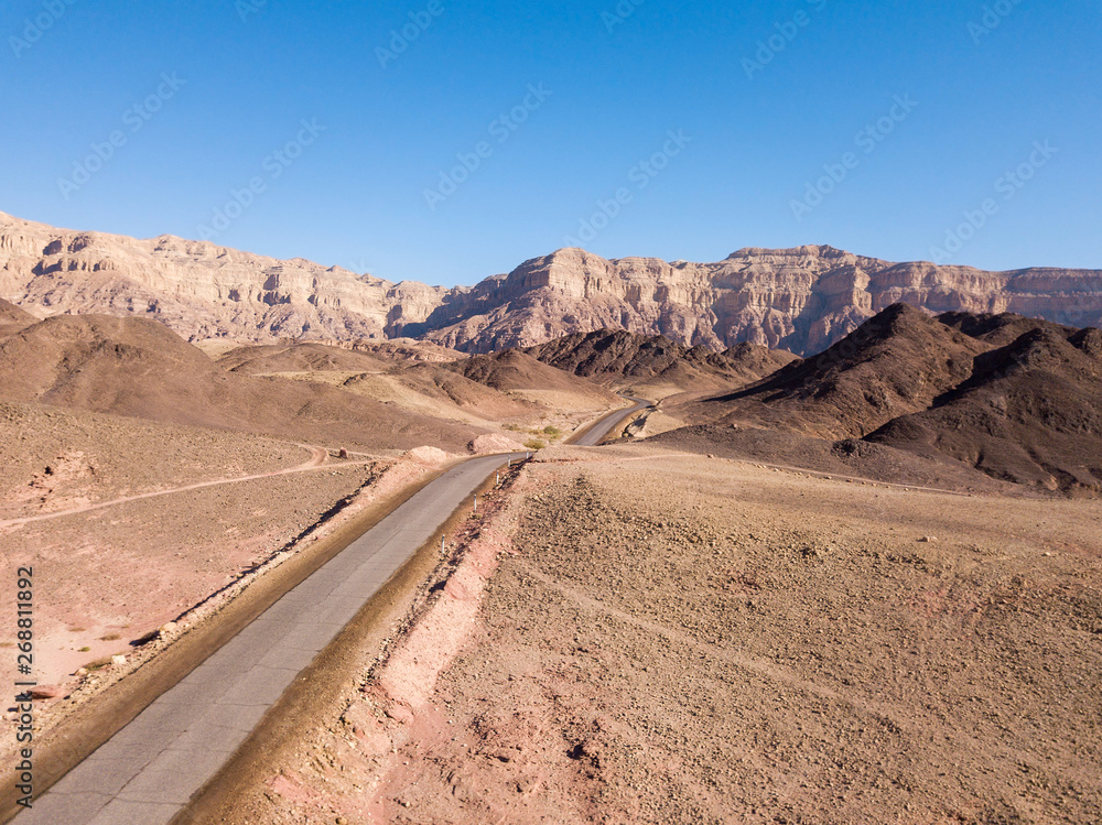 Fototapeta premium Long stretch of an old Desert road with mountains and blue sky in the background, Aerial image.