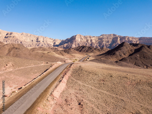 Long stretch of an old Desert road with mountains and blue sky in the background, Aerial image.
