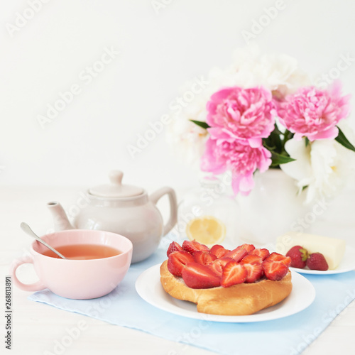 strawberry with croissant and tea on the table near a vase with peonies on a white background