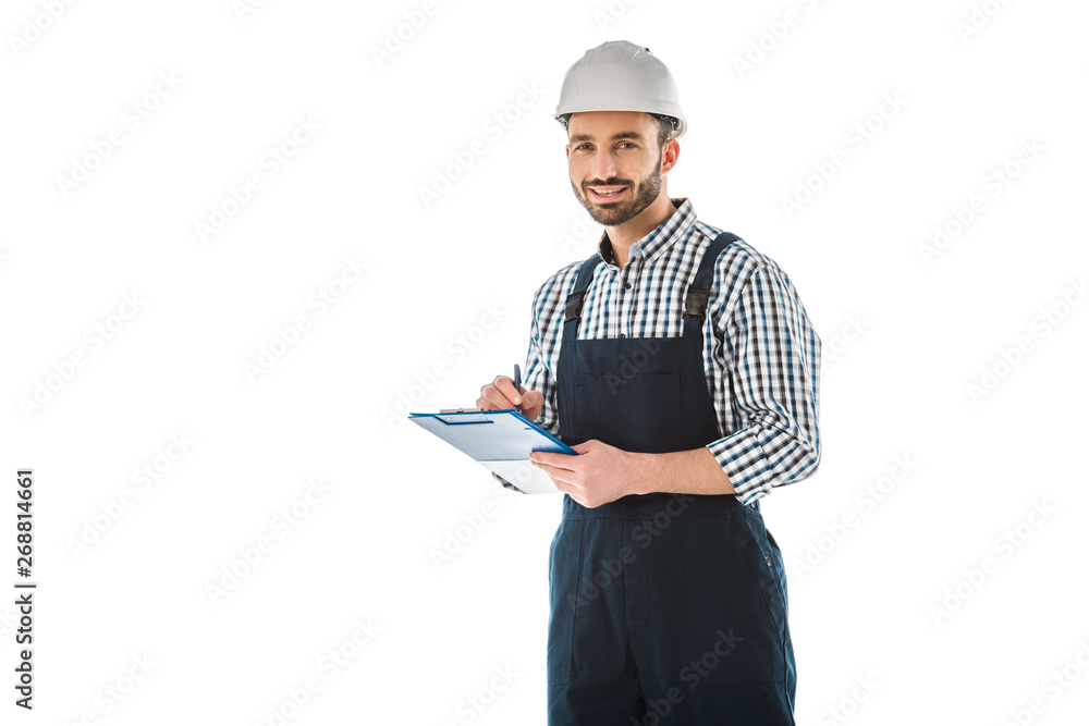 smiling construction worker writing on clipboard and looking at camera isolated on white smiling construction worker writing on clipboard and looking at camera isolated on white