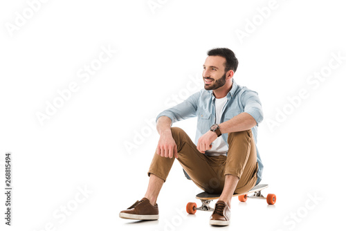 happy man sitting on longboard and looking away isolated on white