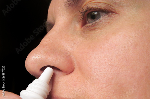 Closeup of middle aged woman dripping nasal drops in nose. Female sprays at home to treat cold, flu or allergy. Health care concept