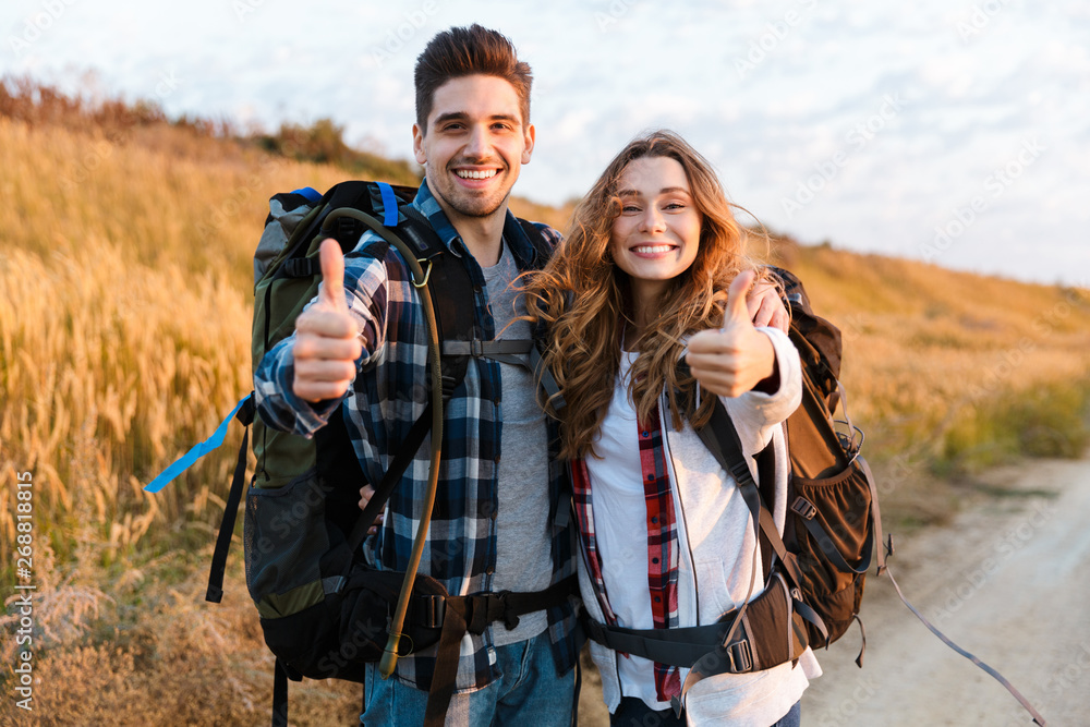 Cheerful young couple carrying backpacks hiking together