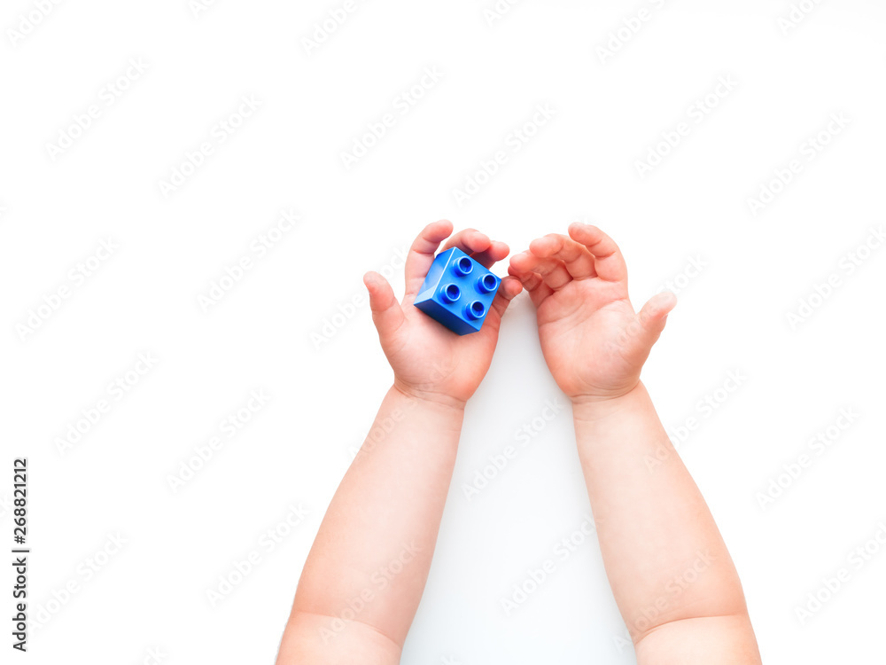 Child is holidng blue constructor block in fist. Kid's hands with toy on white background. Flat lay, top view, copy space.
