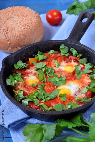 Shakshuka with tomato sauce and quail eggs topped with cilantro in a cast iron pan. Jewish cuisine meal