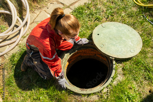 Quadro su tela Girl plumber looks into an open draining manhole