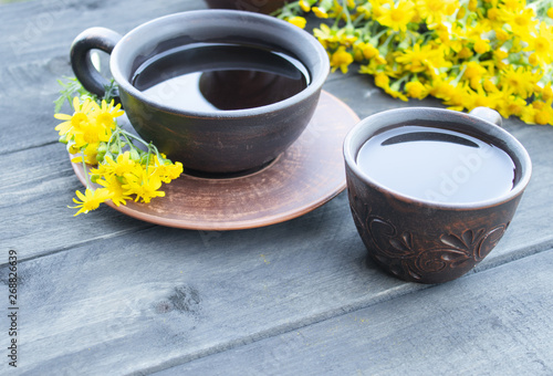Two cups of tea stand on wooden old boards with yellow chamomile flowers.