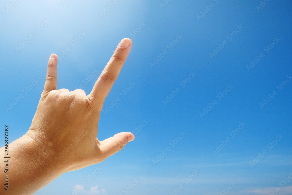 Hand sign of love and showing fingers means I love you on blue sky with sunlight and copty space. Hand sign of love and showing fingers means I love you on blue sky with sunlight and copty space.