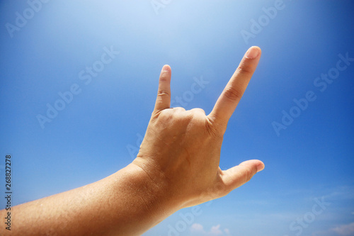 Hand sign of love and showing fingers means I love you on blue sky with sunlight and copty space. © cocorattanakorn