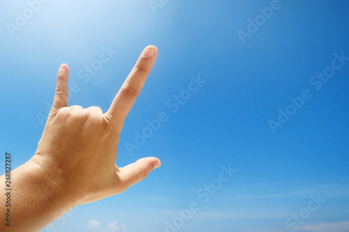Hand sign of love and showing fingers means I love you on blue sky with sunlight and copty space.