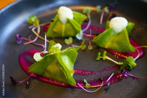 Vegan green raw kimchi dumplings with coconut foam and edible flowers on a black plate