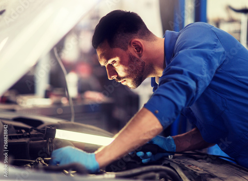 car service, repair, maintenance and people concept - auto mechanic man with lamp working at workshop © Syda Productions