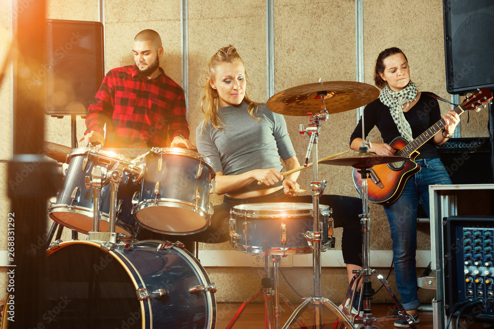 Fototapeta premium Passionate emotional female drummer with her bandmates practicin