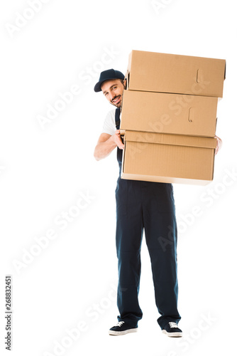 smiling delivery man holding cardboard boxes and looking at camera isolated on white