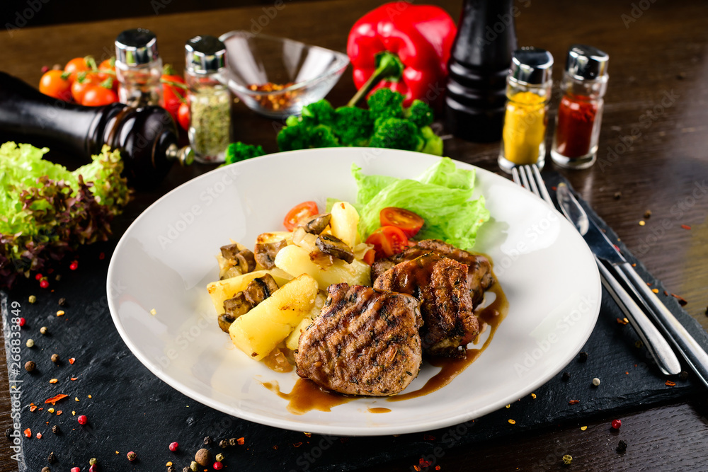 White plate of pork medallions with mushroom sauce on weathered wooden table. White plate of pork medallions with mushroom sauce on weathered wooden table.