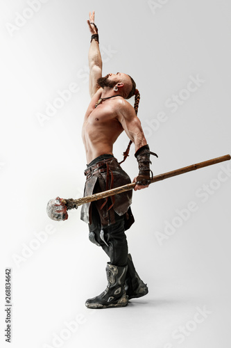 Serious long hair and muscular male model in leather viking's costume with the big mace cosplaying isolated on white studio background. Full-length portrait. Fantasy warrior, antique battle concept. photo