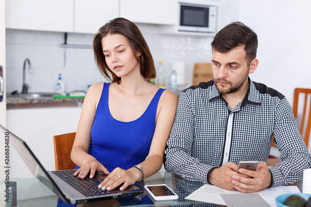Obraz premium Young woman working at laptop and boyfriend using phone at home
