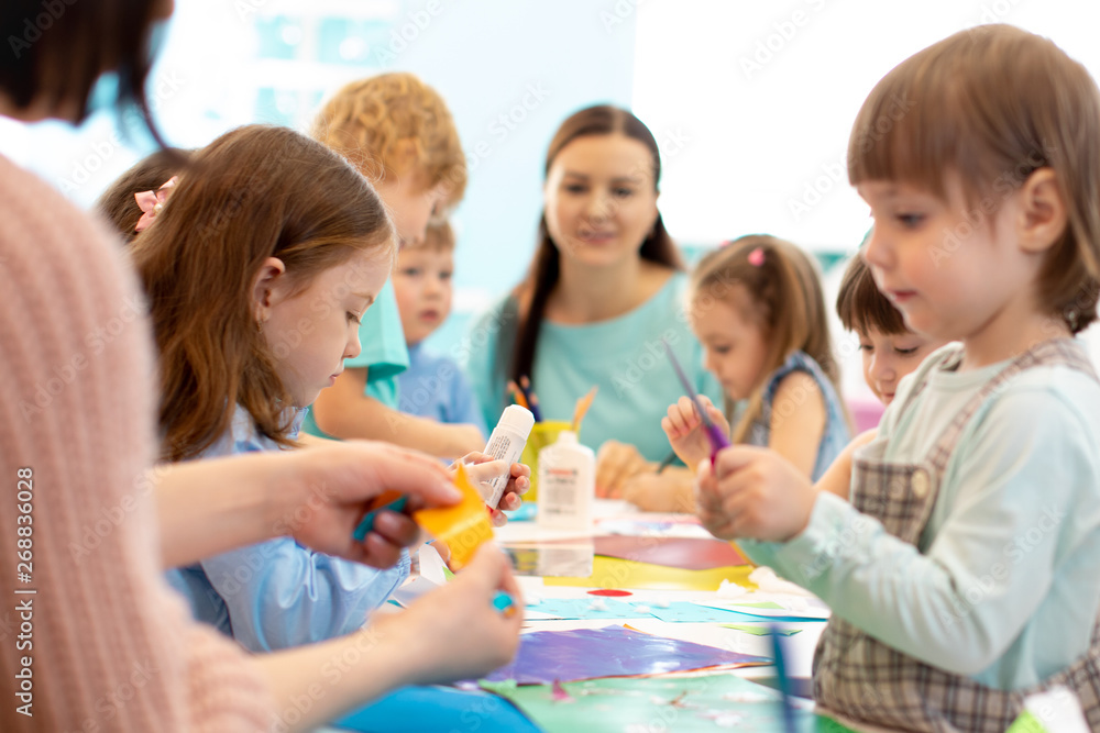 Development learning children in preschool. Children's project in kindergarten. Group of kids and teacher cutting paper and gluing with glue stick on art class in kindergarten or daycare Development learning children in preschool. Children's project in kindergarten. Group of kids and teacher cutting paper and gluing with glue stick on art class in kindergarten or daycare