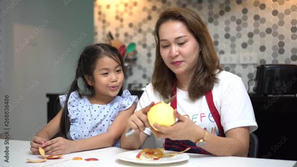 happy Mother teaching daughter peeling red apples together on table in kitchen at home . loving family. child girl excited looking Mom cooking indoors happy Mother teaching daughter peeling red apples together on table in kitchen at home . loving family. child girl excited looking Mom cooking indoors