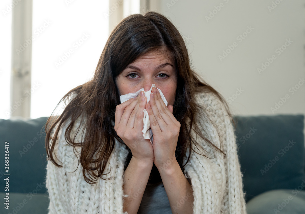Beautiful woman sneezing suffering from cold or allergy feeling awful lying on sofa Beautiful woman sneezing suffering from cold or allergy feeling awful lying on sofa