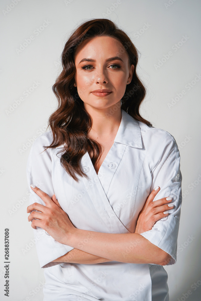Attractive young female doctor in white medical jacket isolated on white background. Portrait of brunette woman cosmetologist with cross hands Attractive young female doctor in white medical jacket isolated on white background. Portrait of brunette woman cosmetologist with cross hands