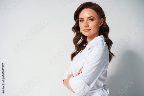 Portrait of attractive young professional female doctor in white medical jacket isolated on white background. Cross hands. Space for text. Medical concept. Healthcare