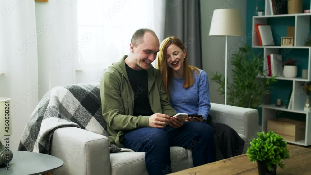 A young couple watching a fun video on a smartphone in their cozy living room A young couple watching a fun video on a smartphone in their cozy living room