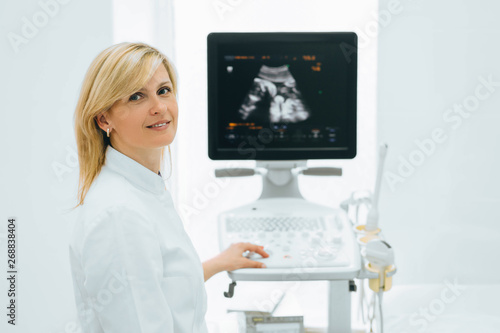 Portrait of smiling Gynecologist sitting by ultrasound machine at her medical office